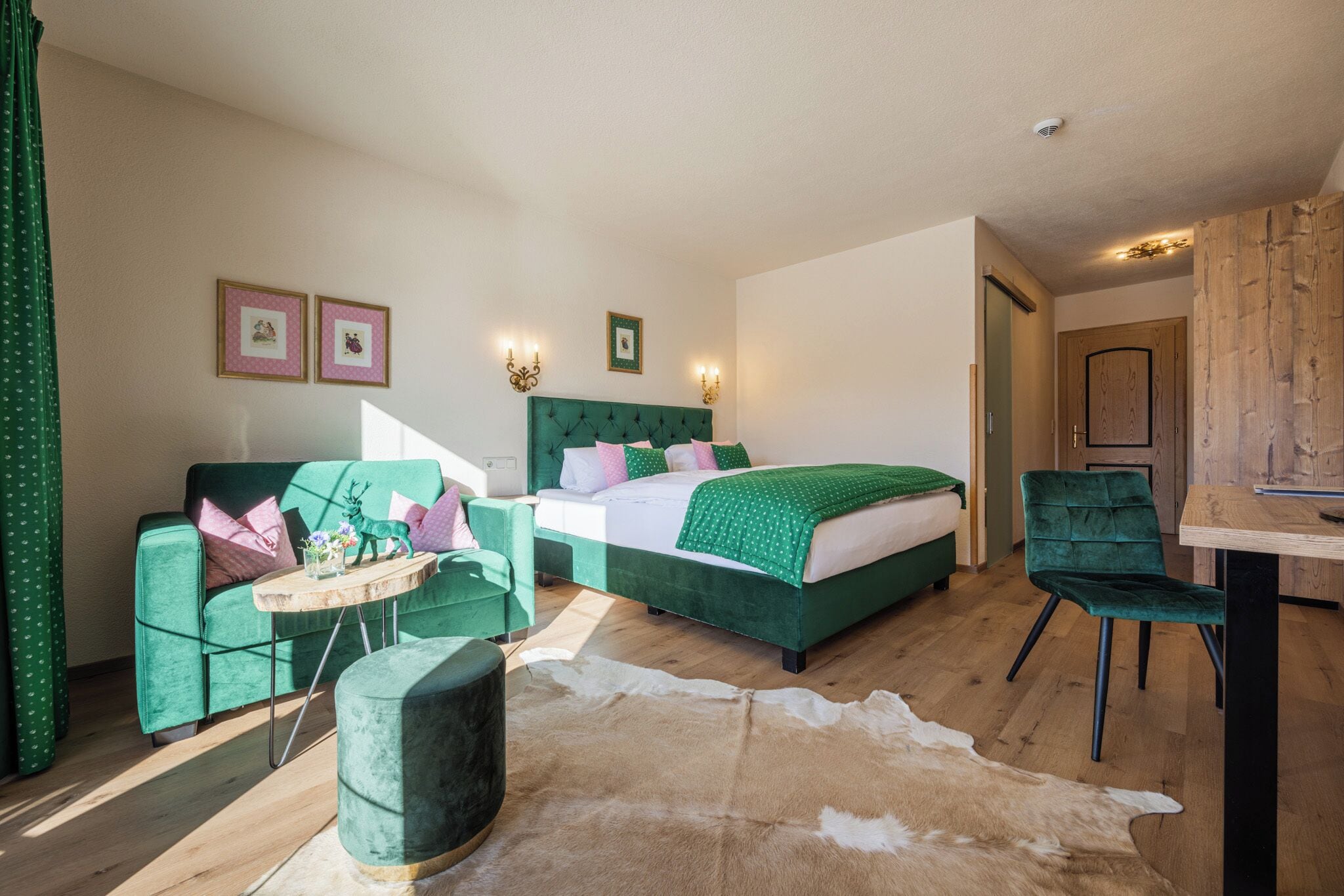 A room with a bed, a green sofa, a wooden table, and a chair.