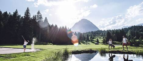 Un campo de golf con una montaña al fondo, un estanque y personas caminando.