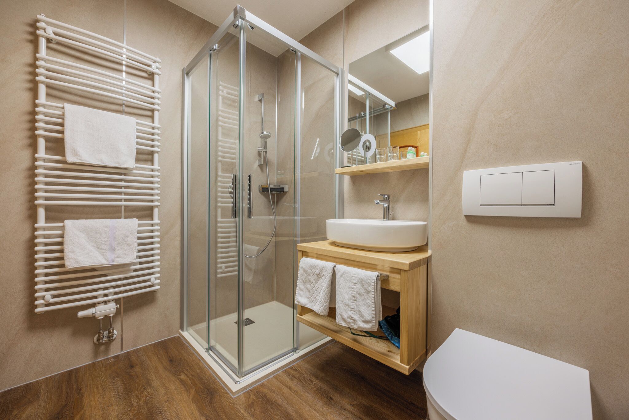 Un baño moderno con ducha envuelta en vidrio, tocador de madera con lavamanos y un inodoro.