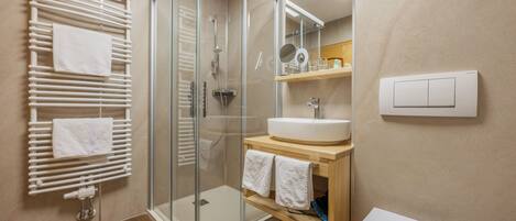Un baño moderno con ducha envuelta en vidrio, tocador de madera con lavamanos y un inodoro.