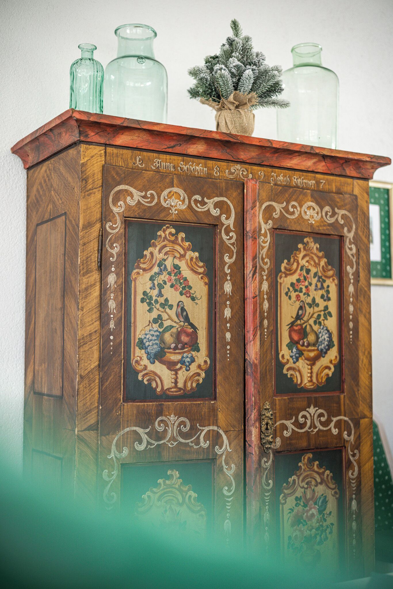 A wooden cabinet with ornate carvings and floral designs, topped with glass bottles and a small plant.