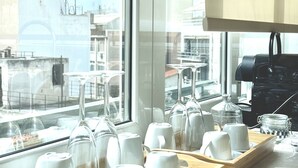 A kitchen with a coffee machine, a window with a view of buildings, and a tray with white cups and glasses.