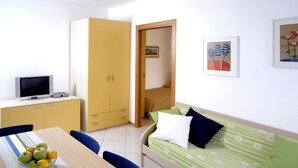 Une pièce de taille modeste comprenant un lit, un bureau avec un ordinateur, une armoire et une table à manger avec des chaises.