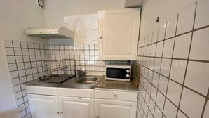 A small kitchen with white cabinets, a stainless steel sink, a microwave, and a gas stove. - Appartement T1 bis Accès Plage à 50m - Rupione (Pietrosella)