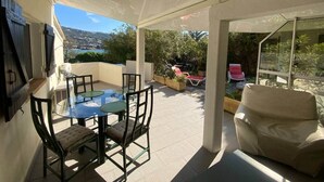 A covered outdoor patio with a glass table and chairs, a beige sofa, and a view of the landscape. - Appartement T1 bis Accès Plage à 50m - Rupione (Pietrosella)