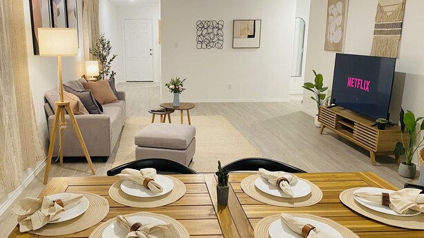 Un salon moderne avec un canapé, une table à manger pour quatre personnes, un téléviseur et une petite table d’appoint sur laquelle est posée une plante.