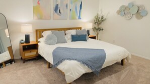 Une chambre à coucher avec un grand lit, deux tables de chevet, un miroir, des œuvres d’art abstraites accrochées au mur et un élément décoratif mural.