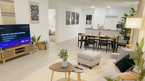 Un salon moderne doté d’un téléviseur à écran plat, d’un coin repas et d’une cuisine.