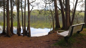 A bench by a calm lake surrounded by trees. - Retro Beach House by HolidayCo. (MACMASTERS BEACH)