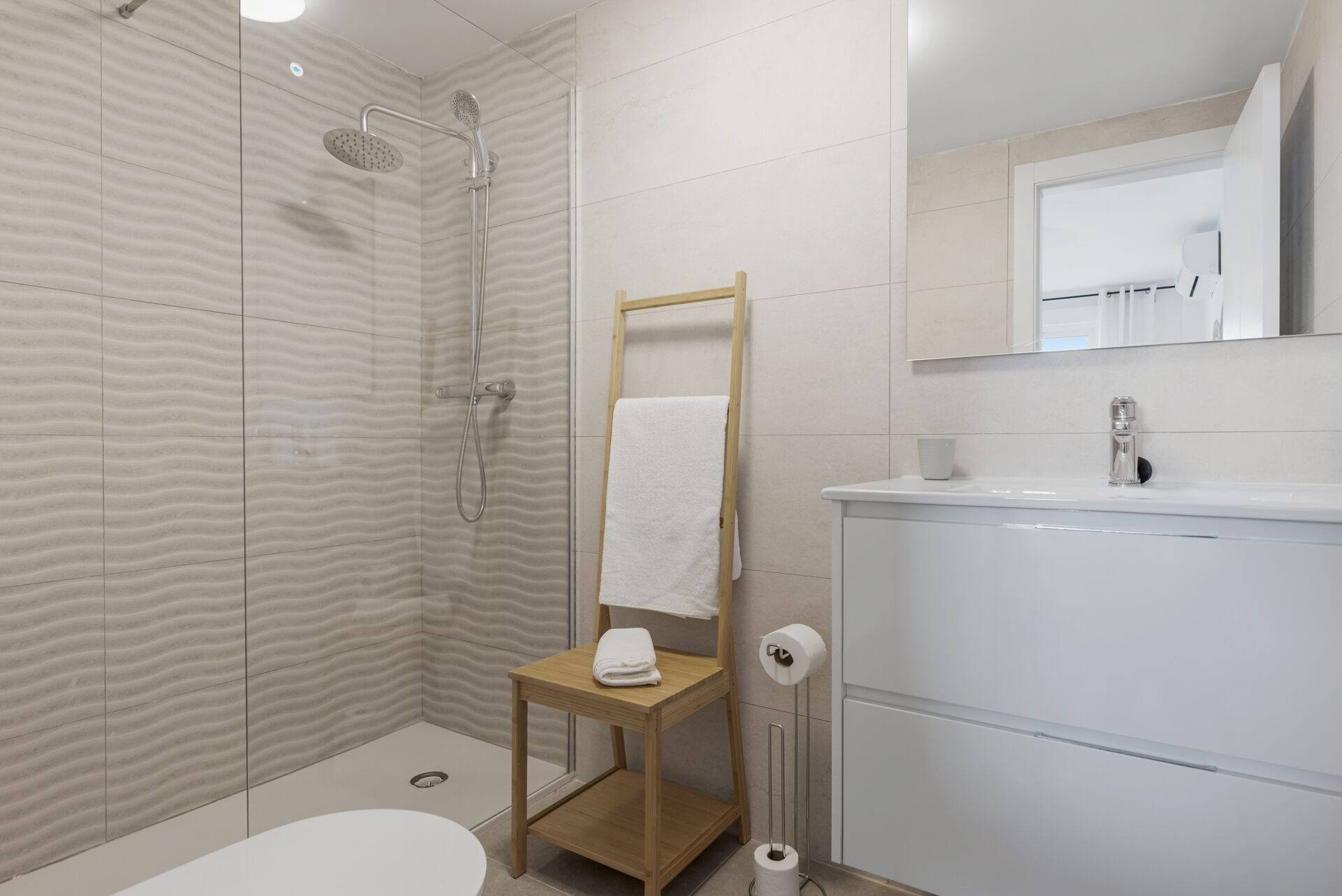 A modern bathroom with a shower, a wooden stool, a toilet, and a sink.