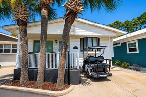 A single-story house with a porch, palm trees, and a golf cart parked in front.