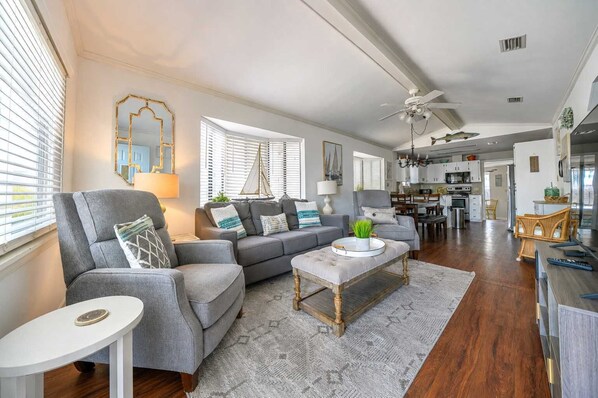 A spacious living room with a grey sofa set, a round coffee table, and a dining area with a chandelier.