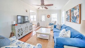 A spacious living room with a television, a white cabinet, a blue sofa, and a ceiling fan.