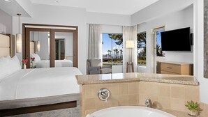 Ein Hotelzimmer mit einem großen Bett, einer Badewanne, einem Fernseher und Blick ins Freie.