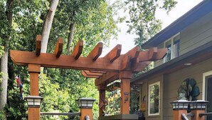 A wooden pergola with a staircase leading to a covered patio area. - Everchanging Seasons: Charming Retreat + Cottage • Hot Tub • Sauna • Game Haven (Burnsville)