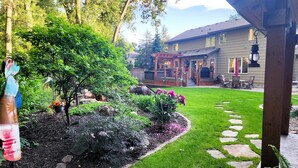 A well-maintained garden with a stone pathway, a wooden pergola, and a house with a porch. - Everchanging Seasons: Charming Retreat + Cottage • Hot Tub • Sauna • Game Haven (Burnsville)