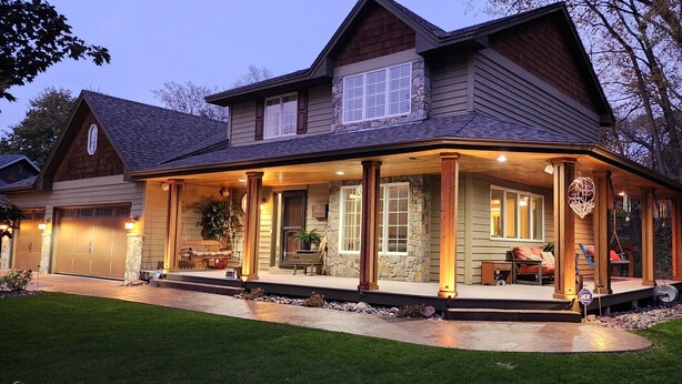 A two-story house with a covered porch, stone accents, and a well-maintained lawn. - Everchanging Seasons: Charming Retreat + Cottage • Hot Tub • Sauna • Game Haven (Burnsville)