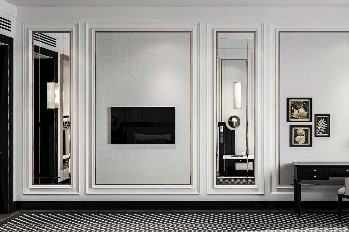 Une chambre d’hôtel dotée d’un grand miroir, d’un téléviseur à écran plat, d’un bureau avec une chaise et d’œuvres d’art encadrées accrochées au mur.