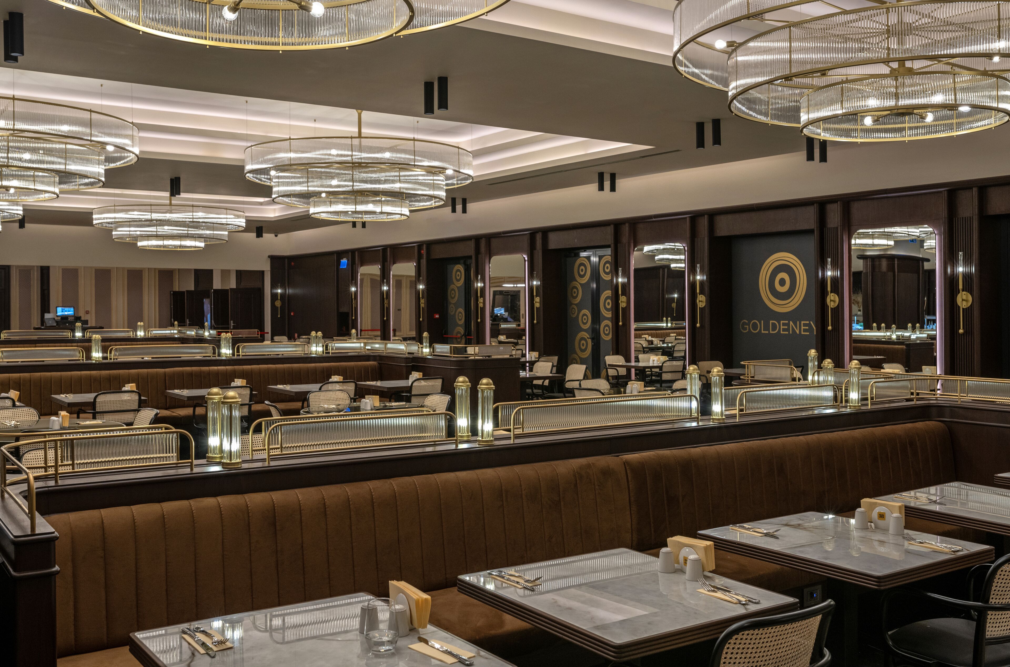 Un restaurante moderno con varias zonas de estar, incluidas mesas y cabinas, y un llamativo letrero que dice 'GOLDENEY'.