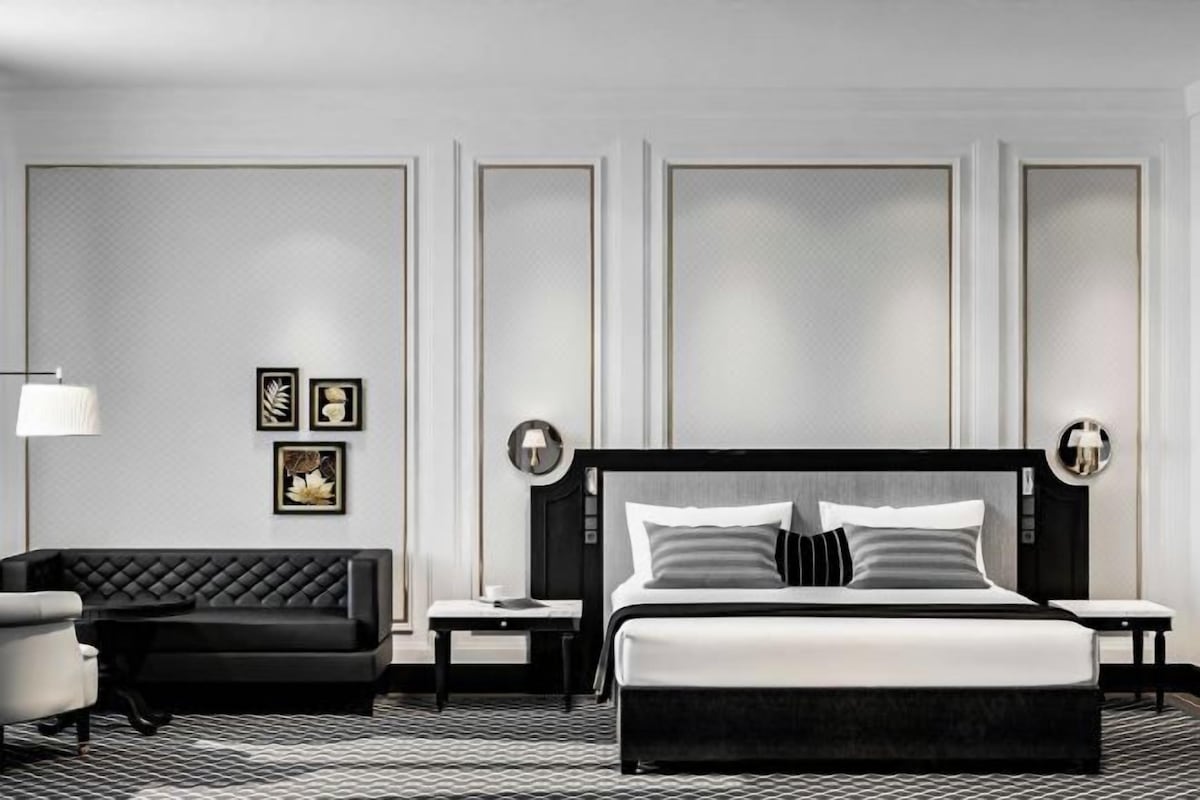 Una habitación de hotel moderna con una cama grande, un sofá negro y una mesita pequeña.
