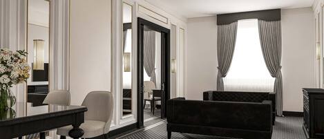 Habitación de hotel con un espejo grande, un sofá negro, una silla, una mesita y un jarrón de flores.