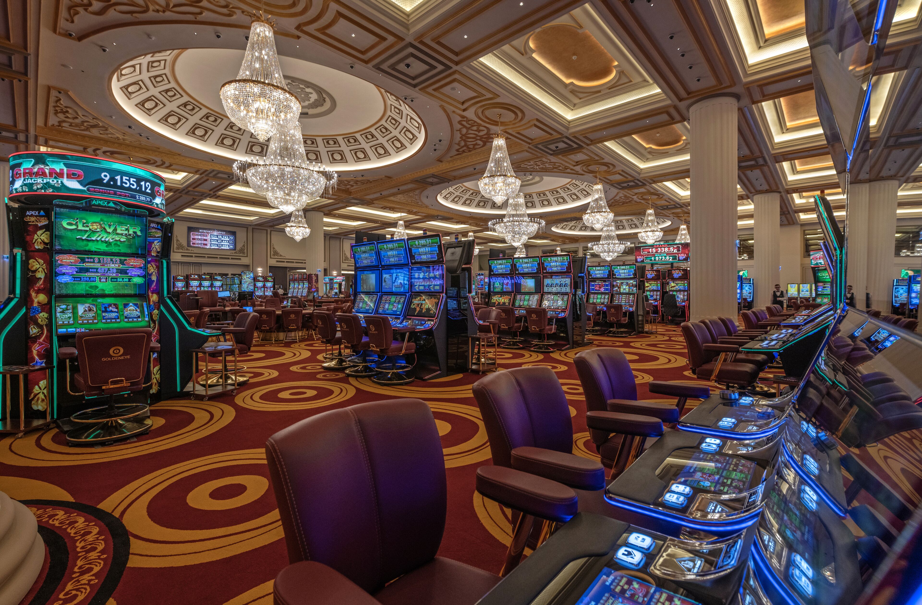 A casino with multiple slot machines, comfortable seating, and ornate ceiling decorations.