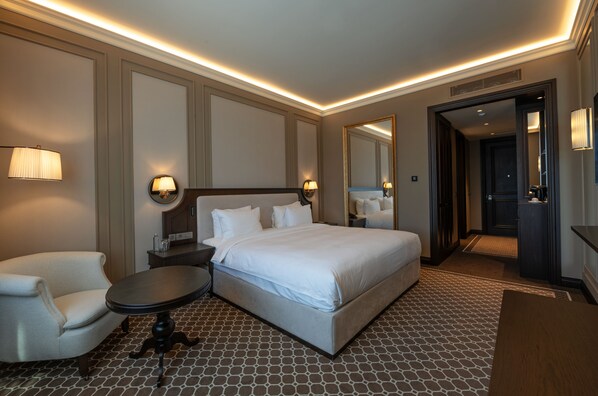 A hotel room with a large bed, a chair, a small table, and a mirror.