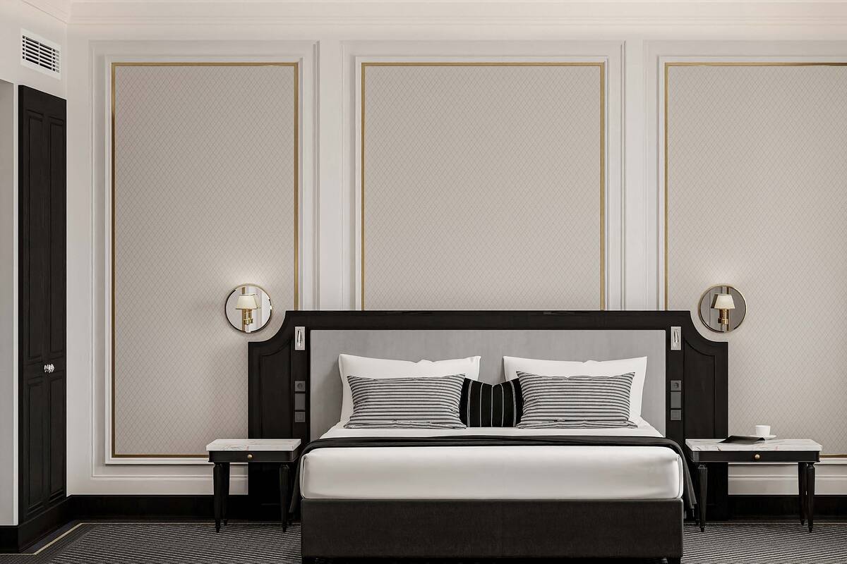 Une chambre d’hôtel avec un grand lit, deux tables de chevet, une petite table, une lampe fixée au mur et une porte.