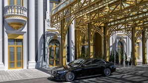 Un coche negro estacionado frente a un edificio con balcones y columnas doradas ornamentales.