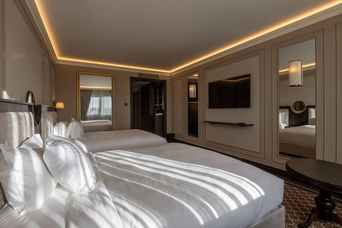 Une chambre d’hôtel avec deux lits, une télévision, un miroir et une petite table.