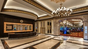 Un lobby lujoso con suelo de mármol, un gran candelabro y una zona de recepción con un espejo grande y una pantalla digital.