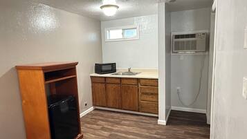 A compact kitchen with wooden cabinets, a black refrigerator, a microwave, and a window above the sink.