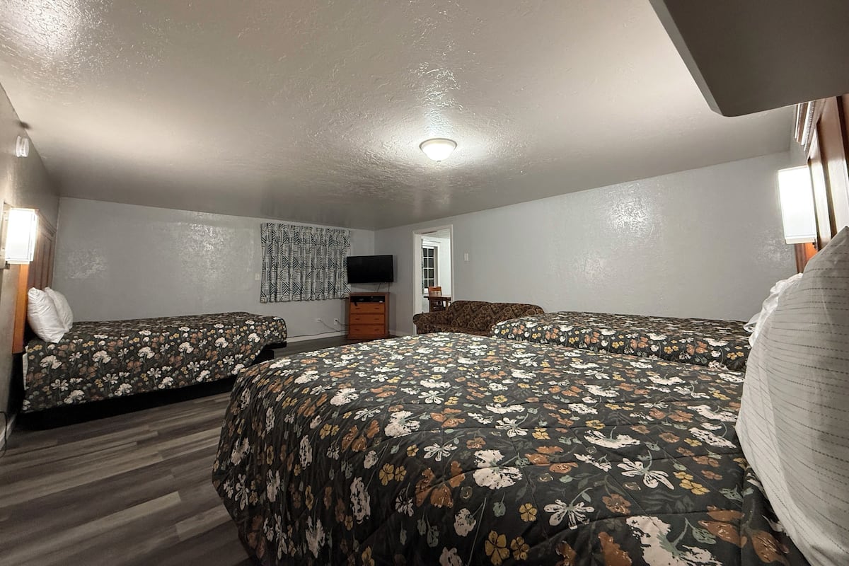 A hotel room with two beds, a TV, a wooden dresser, and a small seating area.