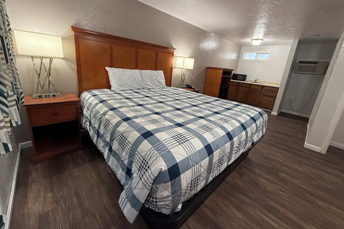 A bedroom with a bed, nightstands, a wooden headboard, a desk with a chair, a television, and a wardrobe.