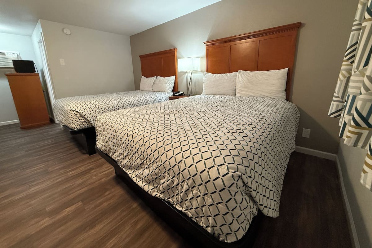A bedroom with two beds, a wooden headboard, a bedside table, and a lamp.