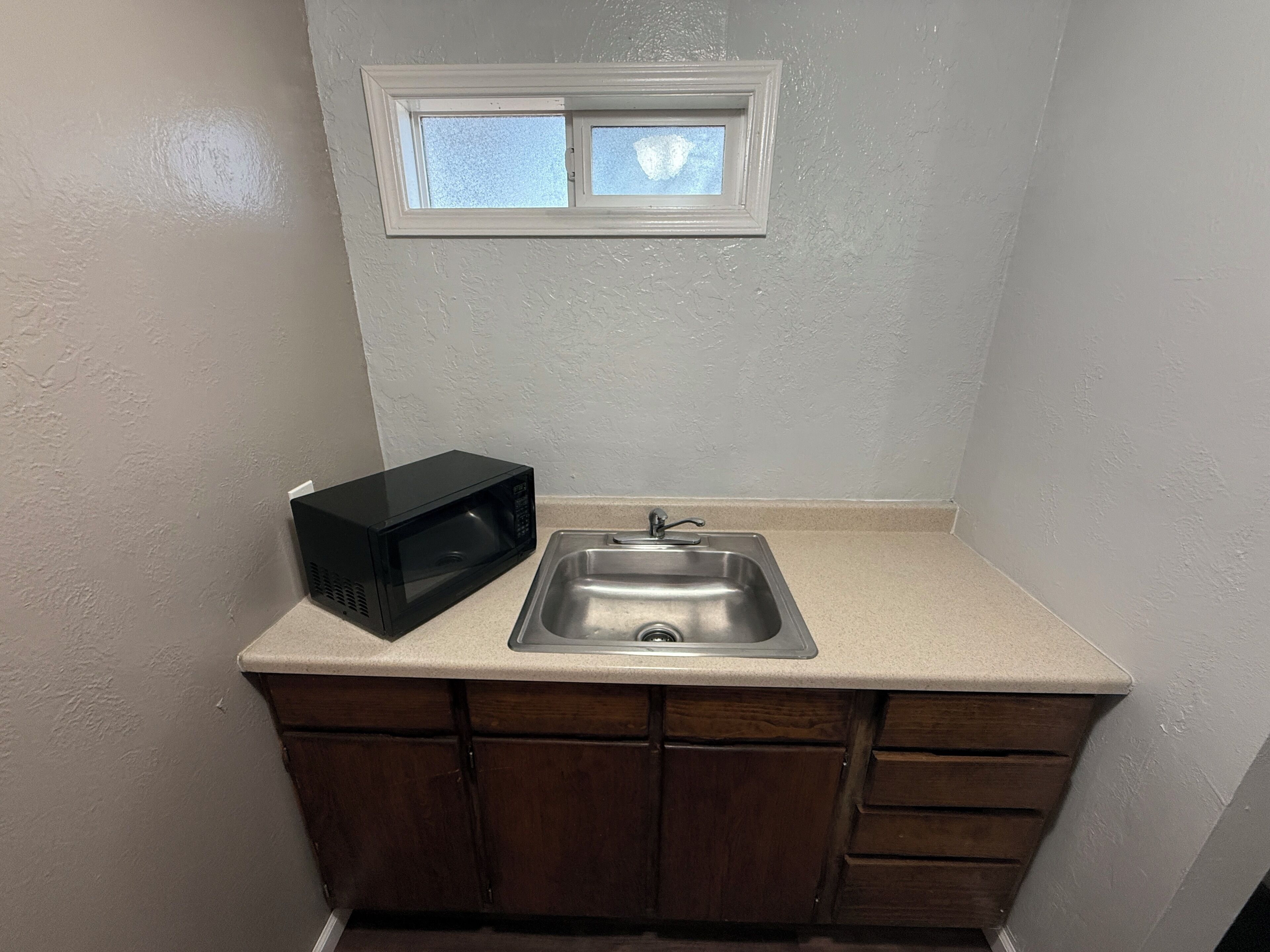 A small kitchenette with a microwave, sink, and window above the countertop.