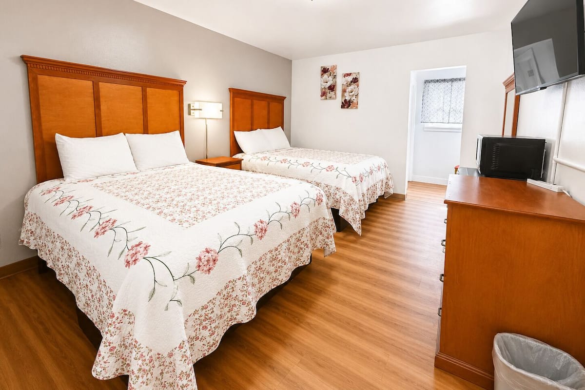 A hotel room with two beds, a desk, a TV, and a window.