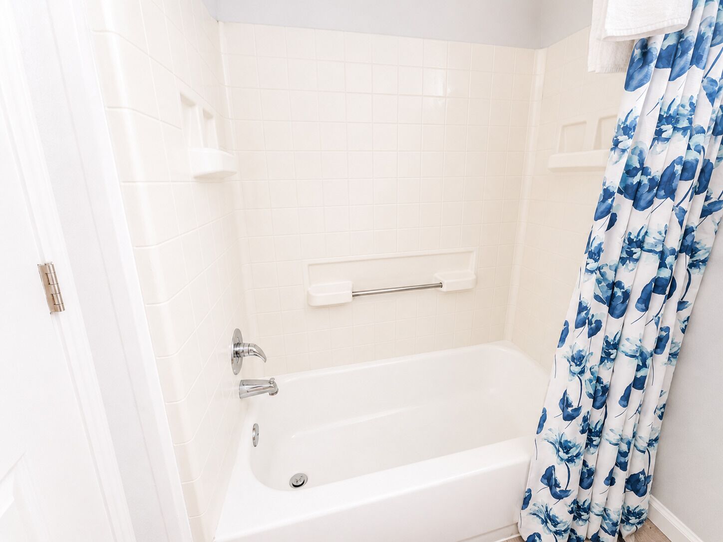 Une salle de bain avec une baignoire blanche, un rideau de douche orné d’un motif floral bleu et un porte-serviettes blanc.