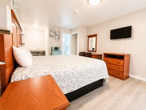 A bedroom with a bed, a wooden dresser, a television, and a bathroom visible in the background. - Royal Gateway Motel (Bend)