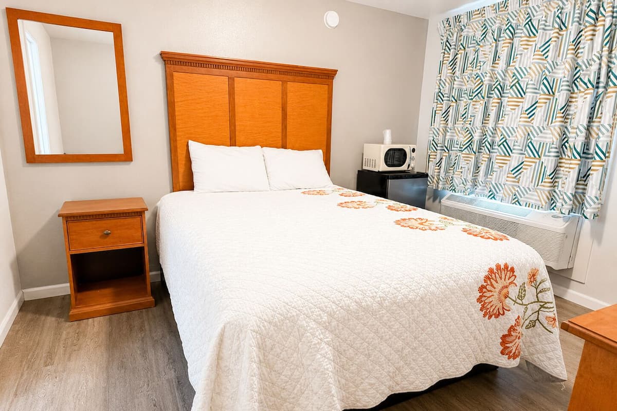 A bedroom with a bed, a nightstand, a mirror, a heater, and a window with curtains.