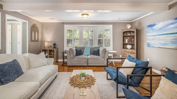 A living room with a sofa, armchair, coffee table, and a painting on the wall. - Spacious 4br/3ba Park Circle Home. Great Location! (North Charleston)