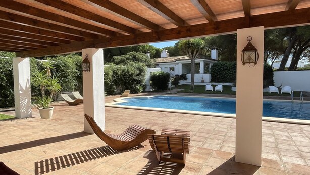 Un espacio al aire libre cubierto con piscina, muebles de madera y plantas en macetas.