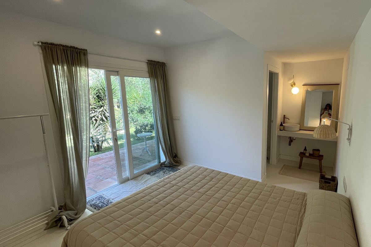 Une chambre avec un lit, une salle de bain avec un lavabo et un miroir, et une porte-fenêtre coulissante donnant sur une terrasse.