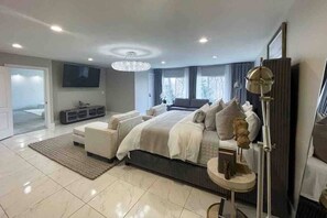 Quarto moderno com uma cama grande, televisão, candelabro e vista para o exterior.