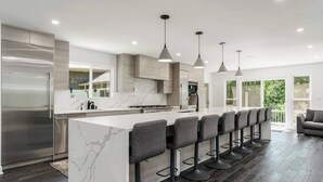 A modern kitchen with a marble island, bar stools, pendant lights, and a stainless steel refrigerator.