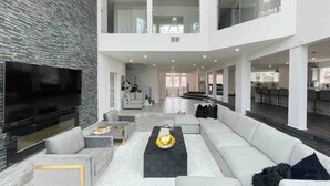 A spacious living area with a large flat-screen TV, a sectional sofa, and a staircase leading to an upper level.