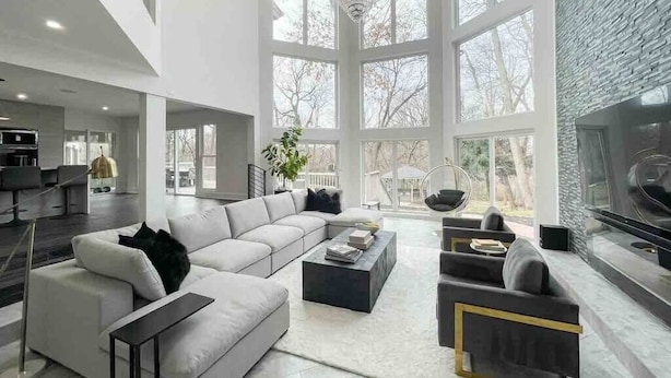 A modern living room with a sectional sofa, a coffee table, a fireplace, and large windows.