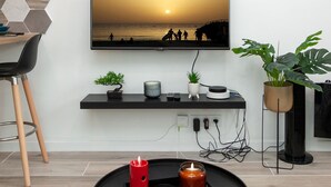 Een moderne woonkamer met een flatscreen televisie aan de muur, een zwarte salontafel met kaarsen, een klein plantje en een potplant op een standaard.