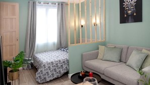 Een kamer met een bed, een slaapbank, een raam met gordijnen, een wandlamp en een schilderij.