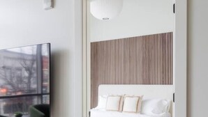 A modern bedroom with a white bed, a mounted TV, and a wooden slat headboard. - Modern Luxury in Downtown TC (Traverse City)